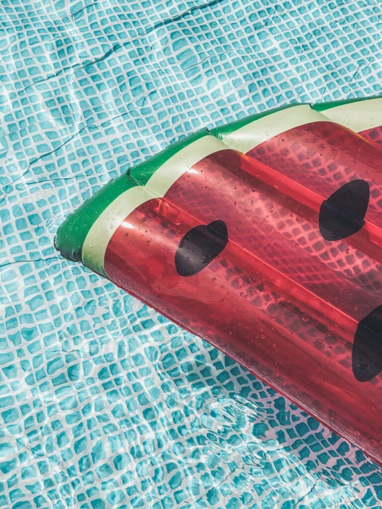 A vibrant watermelon-shaped inflatable float on clear blue water in a swimming pool, perfect for summer leisure.
